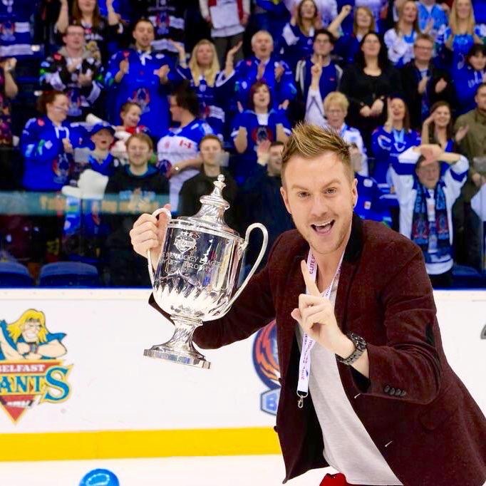 JD on the ice with a championship trophy, crowd behind him in Blaze blue