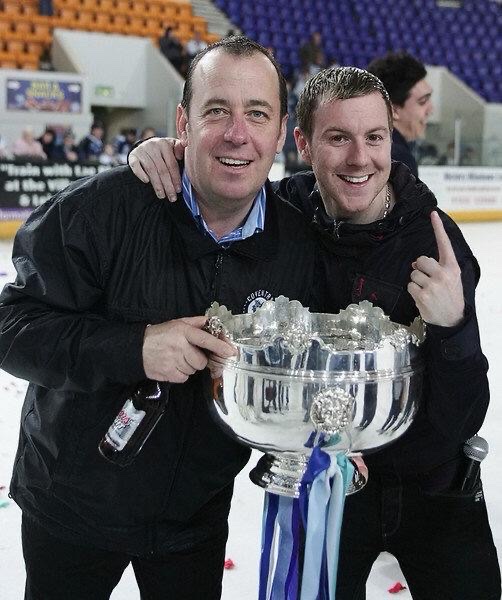 JD and a teammate on the ice with the trophy, microphone in his pocket